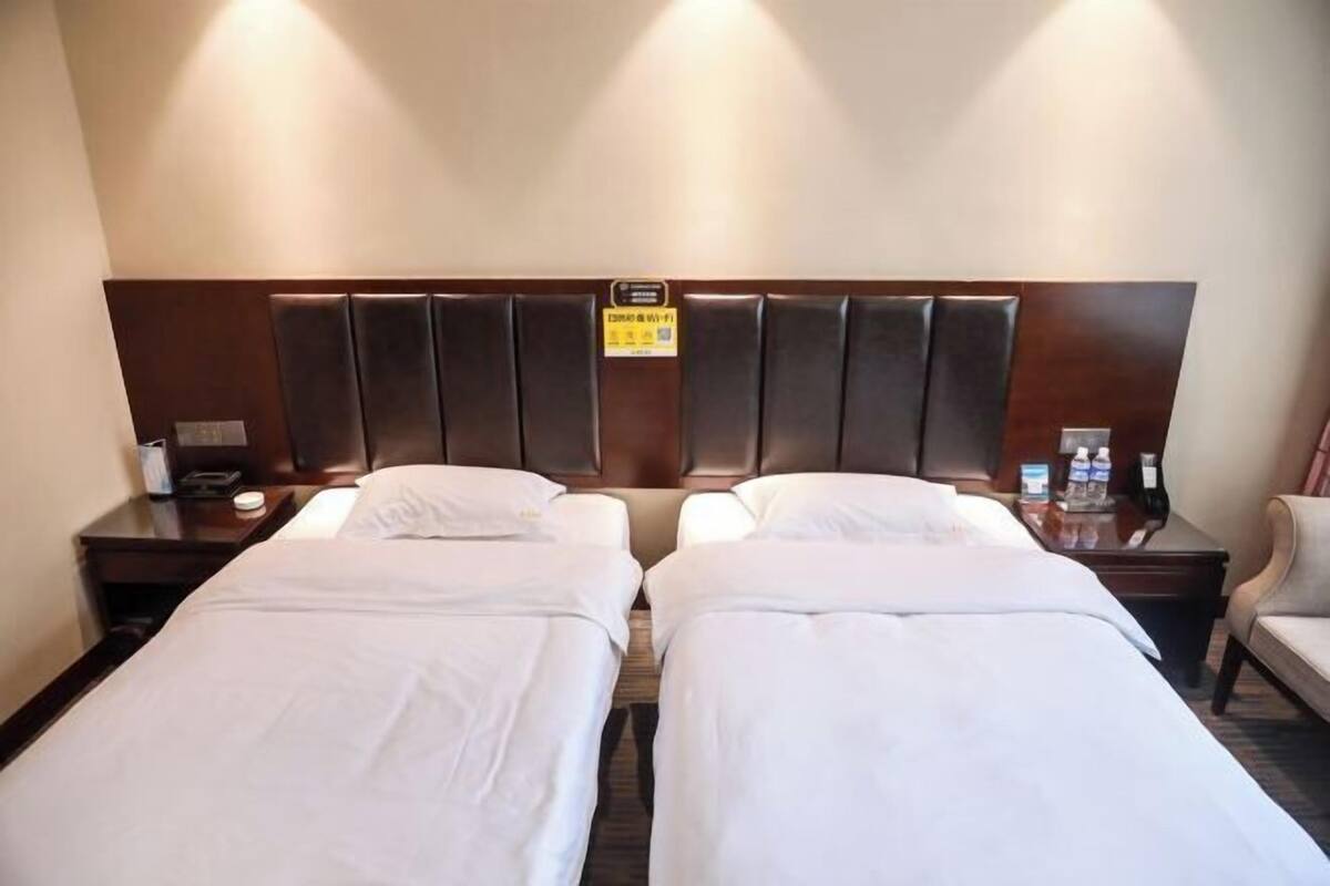 Une chambre d’hôtel avec deux lits simples, une tête de lit en bois, une table de chevet avec un téléphone et une lampe, et une chaise.