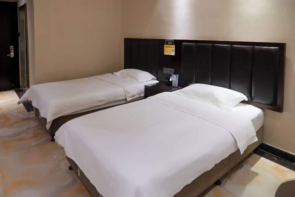 Une chambre d’hôtel avec deux lits, une tête de lit sombre, une petite table et une porte.