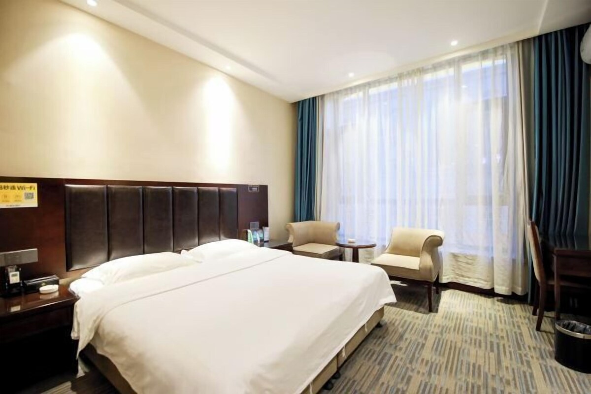 A hotel room with a large bed, a desk, a chair, and a window with curtains.
