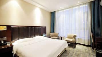 Habitación de hotel con una cama grande, un escritorio, una silla y un ventanal con cortinas.