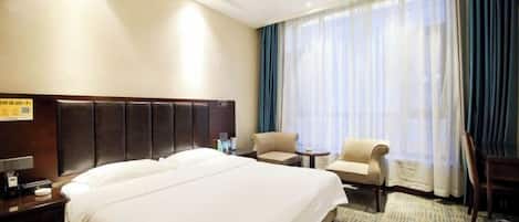 A hotel room with a large bed, a desk, a chair, and a window with curtains.