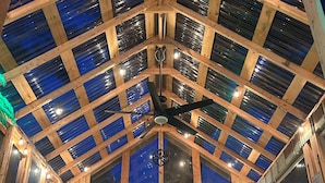 Une terrasse couverte avec un plafond en bois et des panneaux de verre, une table avec des chaises et un ventilateur de plafond.
