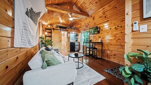 A cozy wooden cabin interior with a sofa, a small table, and a ceiling fan. - Hot Tub! Tiny House Retreat in the Woods (Stanton)