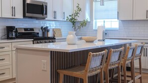 A modern kitchen with white cabinetry, a central island with bar stools, stainless steel appliances, and pendant lighting. - New Home, Walk to Clinic, Private Patio & Hot Tub! (Cleveland)