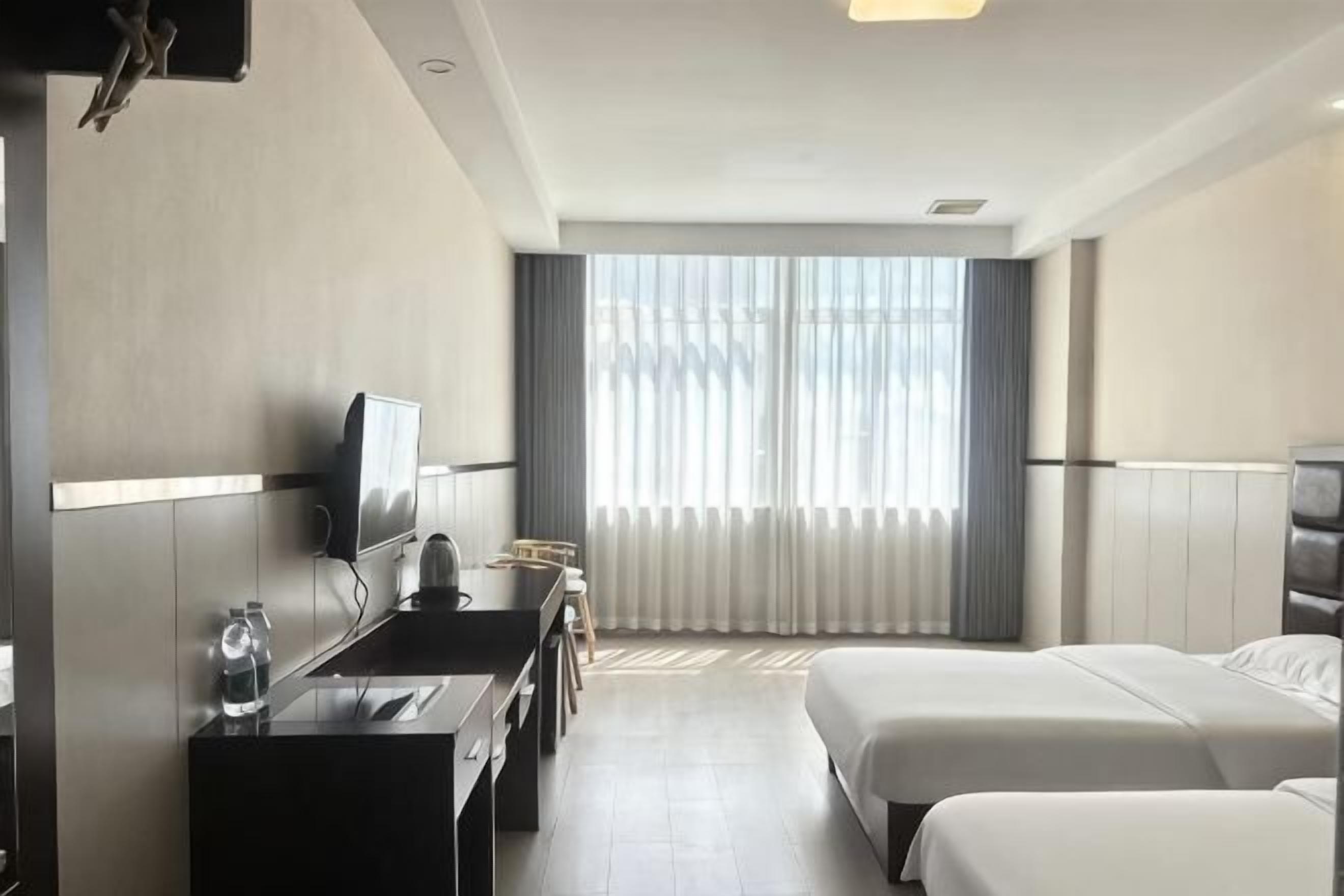 A hotel room with a bed, a desk with a chair, a television, and a window with blinds.