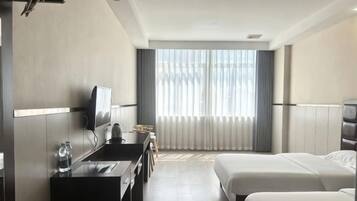 A hotel room with a bed, a desk with a chair, a television, and a window with blinds.