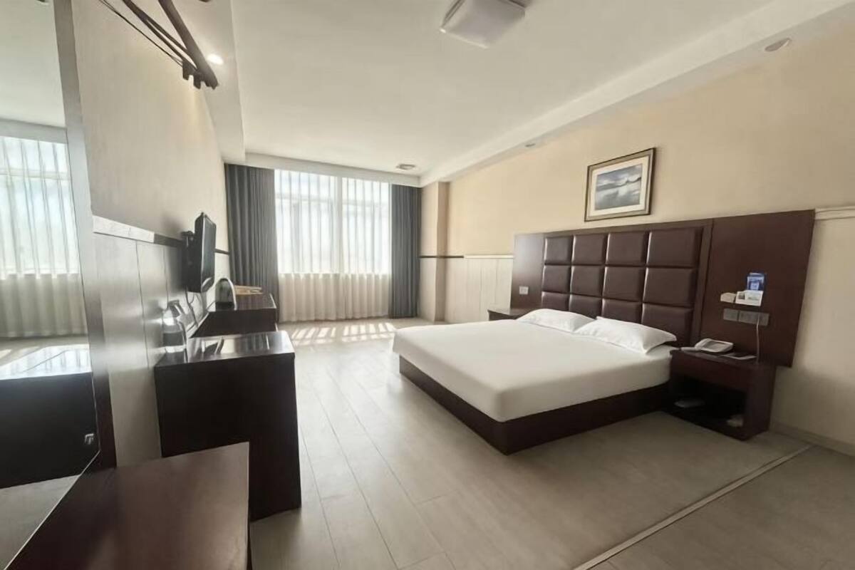 Quarto de hotel com cama, secretária, cadeira, televisão e janela com cortinas.
