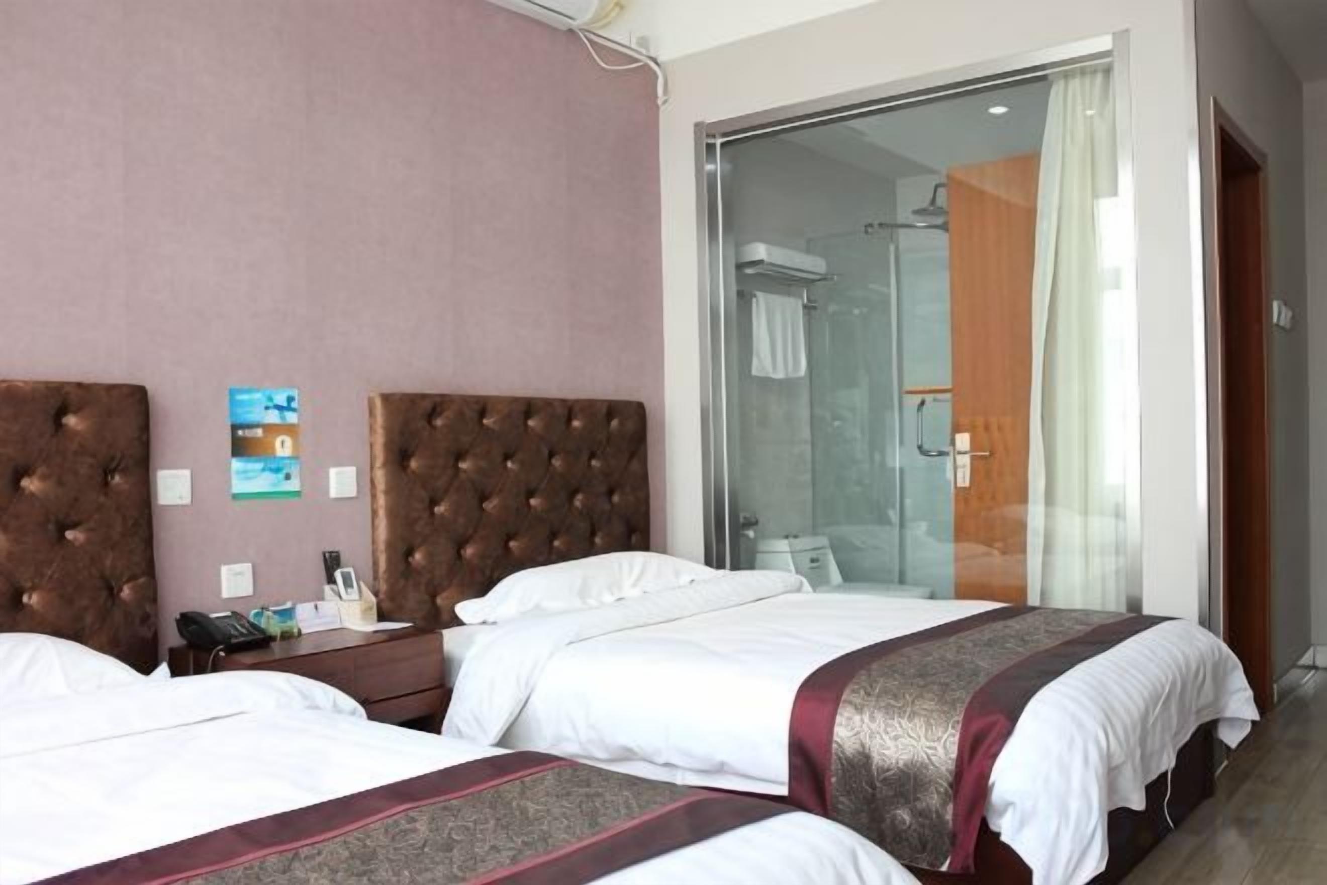 Quarto de hotel com duas camas, divisória de chuveiro de vidro e cabeceira de madeira.