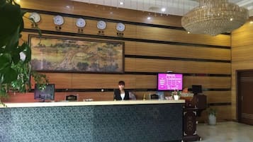 Un mostrador de recepción con una pantalla digital, relojes y un cuadro grande en la pared.