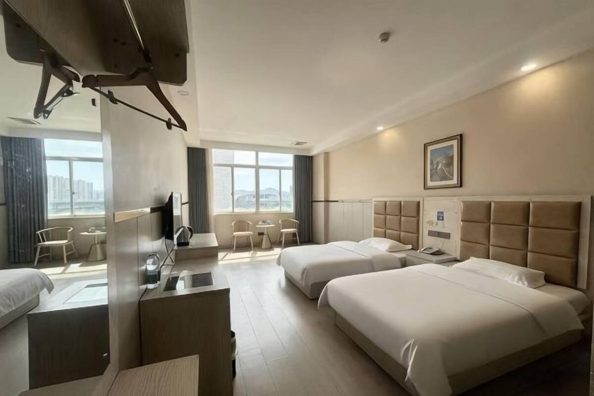Quarto de hotel com duas camas, uma mesa, uma cadeira, uma televisão e janela com vista para a cidade.