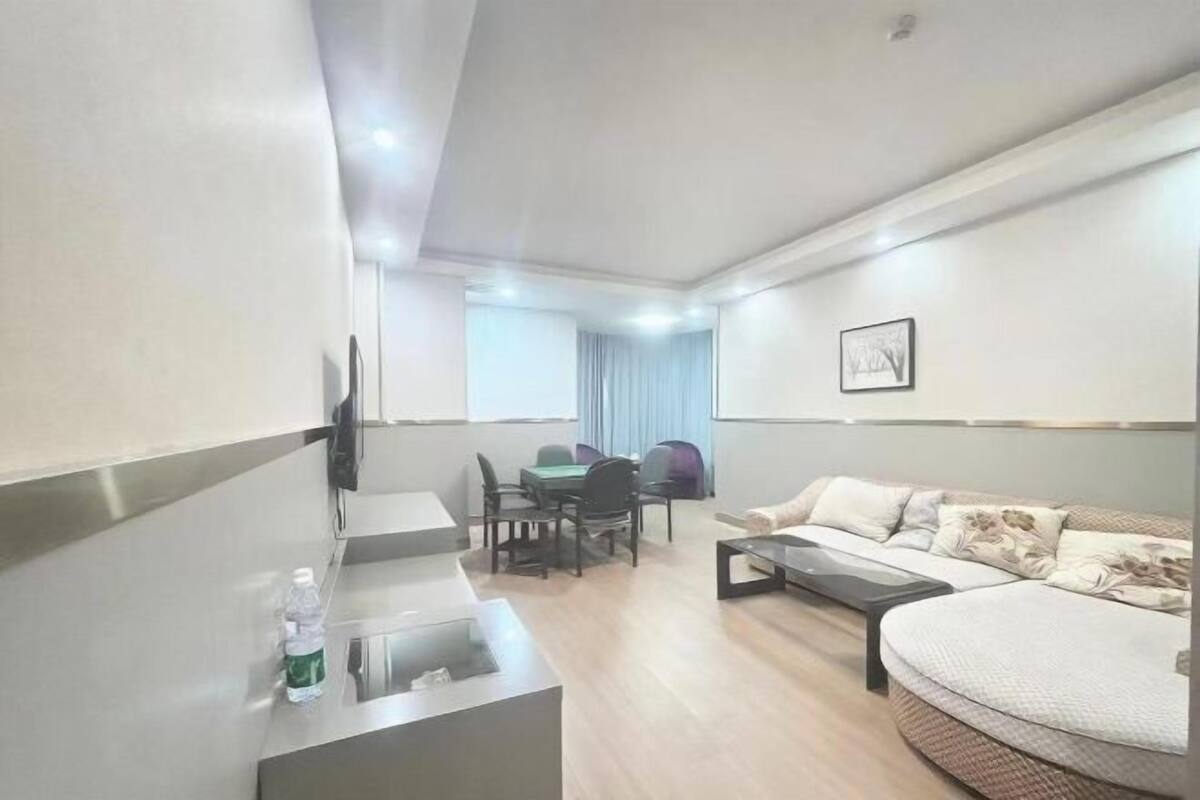 Uma sala de estar moderna com um sofá, uma mesa de centro, uma televisão na parede e um espaço de jantar com cadeiras e uma mesa.