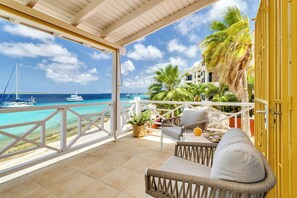 Ein Balkon mit Blick auf das Meer und Boote, ein Korbstuhl, ein Tisch mit einer Pflanze und ein gelbes Tor.