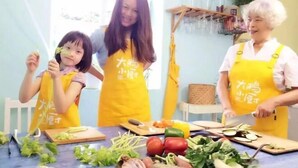Three people wearing yellow aprons with Chinese characters, preparing food with vegetables and a knife on a table. - Me Town House (Shenzhen)