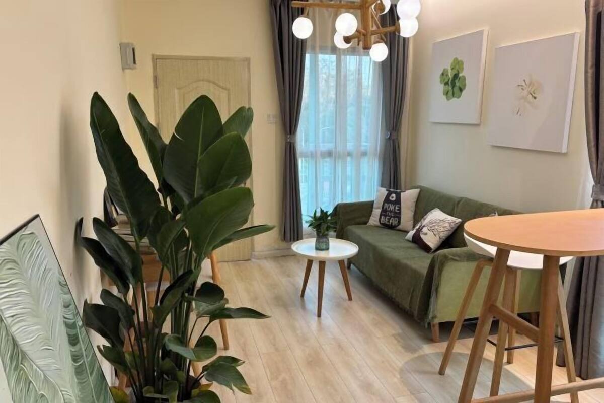 A living room with a green sofa, a round wooden table, and a potted plant.