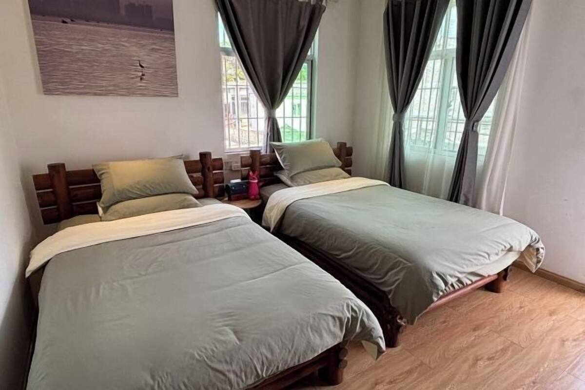 A room with two beds, wooden headboards, and a window with curtains.