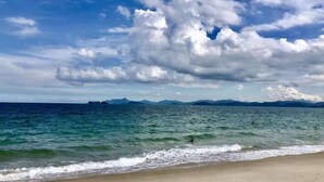 A beach with waves, a clear sky, and distant mountains. - Me Town House (Shenzhen)