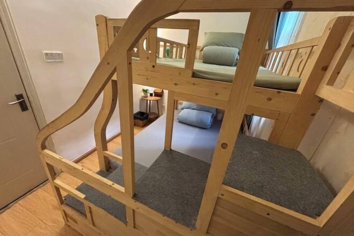 A wooden bunk bed with a ladder, a small table, and a chair in a room with a door and a window.