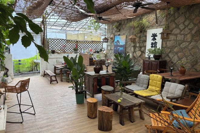 A spacious outdoor seating area with wooden furniture, potted plants, and a stone wall backdrop.