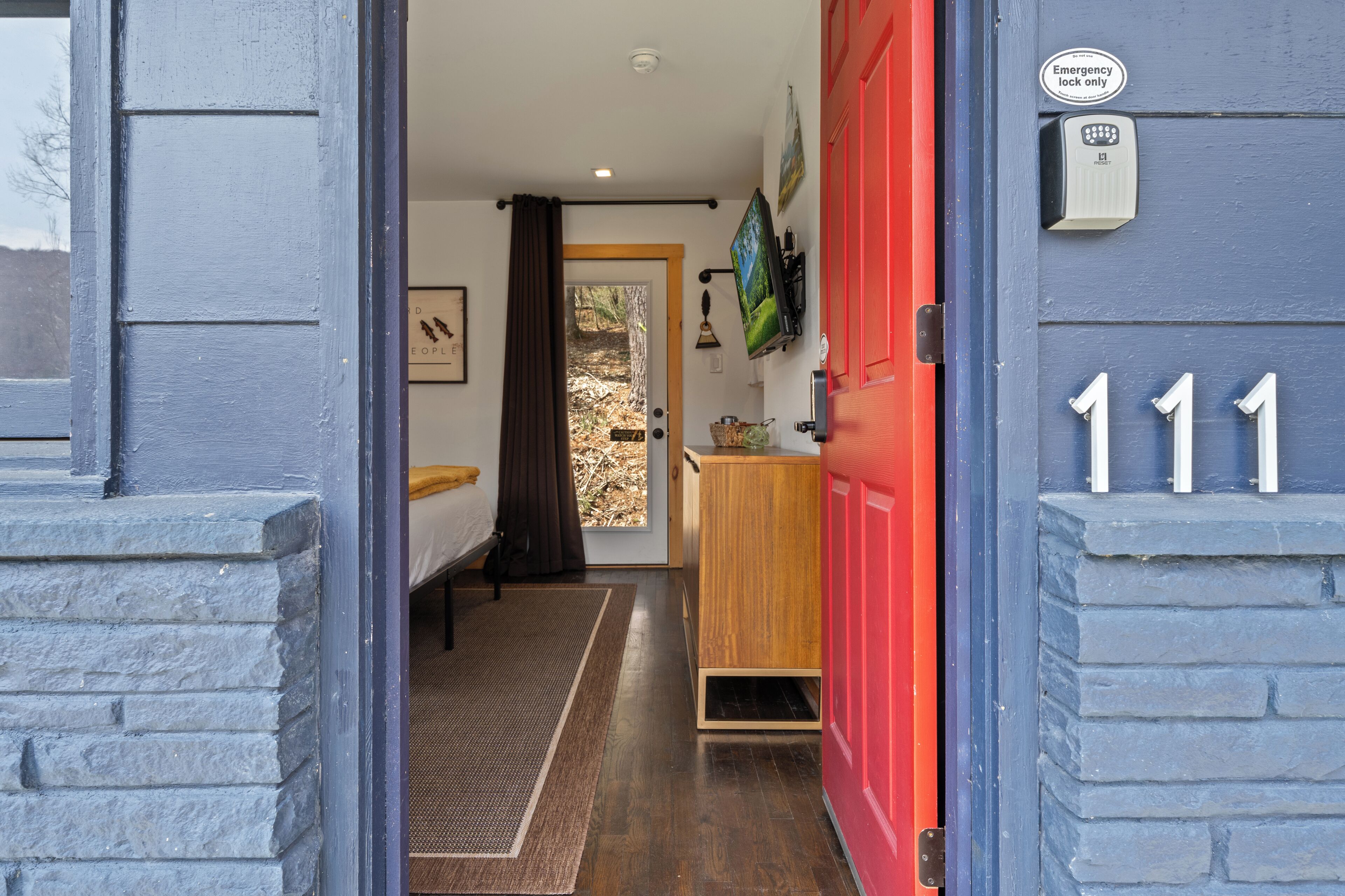 A hallway leading to a bedroom with a bed, a wooden cabinet, and a red door marked with the number 111.