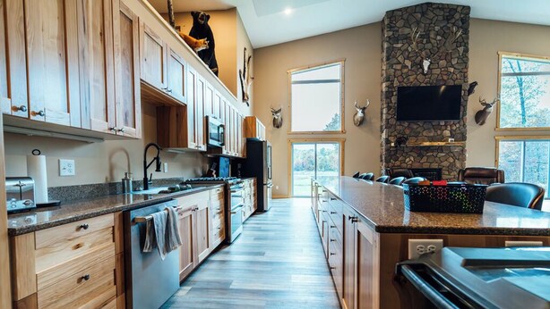 A spacious kitchen with wooden cabinets, a stone fireplace, and a large island. - The Lodge at Nature Shores (Pine City)