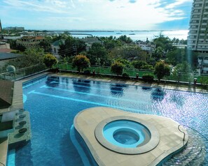 A swimming pool with a hot tub, surrounded by greenery and overlooking a body of water.