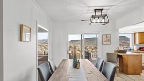 A dining area with a wooden table, chairs, and a view of a mountainous landscape through large windows. - St George Vacation Rental| Condo sleeps 8 guest with Resort Amenities (St. George)
