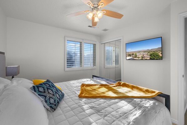 A bedroom with a bed, a ceiling fan, a large window, and a wall-mounted TV. - St George Vacation Rental| Condo sleeps 8 guest with Resort Amenities (St. George)