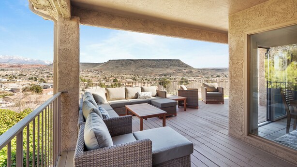 A covered outdoor seating area with a sofa, chairs, and a table, overlooking a mountainous landscape. - St George Vacation Rental| Condo sleeps 8 guest with Resort Amenities (St. George)