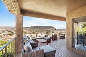 A covered outdoor seating area with a sofa, chairs, and a table, overlooking a mountainous landscape. - St George Vacation Rental| Condo sleeps 8 guest with Resort Amenities (St. George)