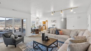 A spacious living room with a large sofa, a coffee table, and a view of a mountainous landscape through large sliding doors. - St George Vacation Rental| Condo sleeps 8 guest with Resort Amenities (St. George)