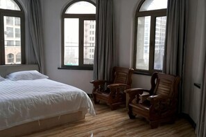 Un dormitorio con una cama grande, dos sillas de madera y tres ventanas.