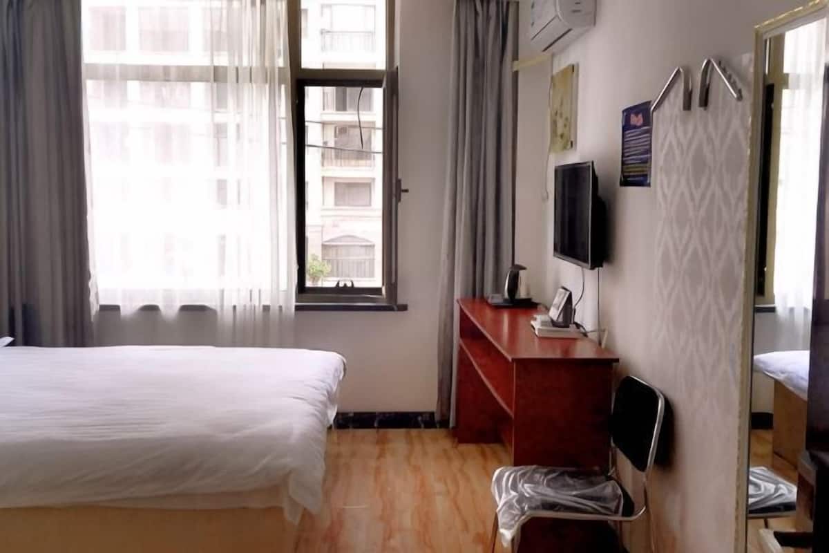 Habitación de hotel con cama, escritorio, silla, televisión y ventana con cortinas.