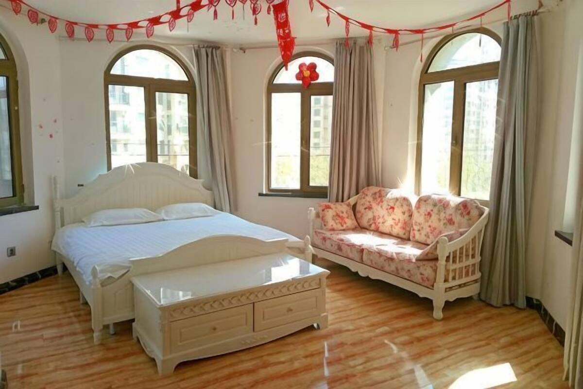 Un dormitorio con cama, sofá y ventanas amplias.