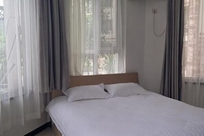 Un dormitorio con cama, cortinas, una ventana y un teléfono instalado en la pared.