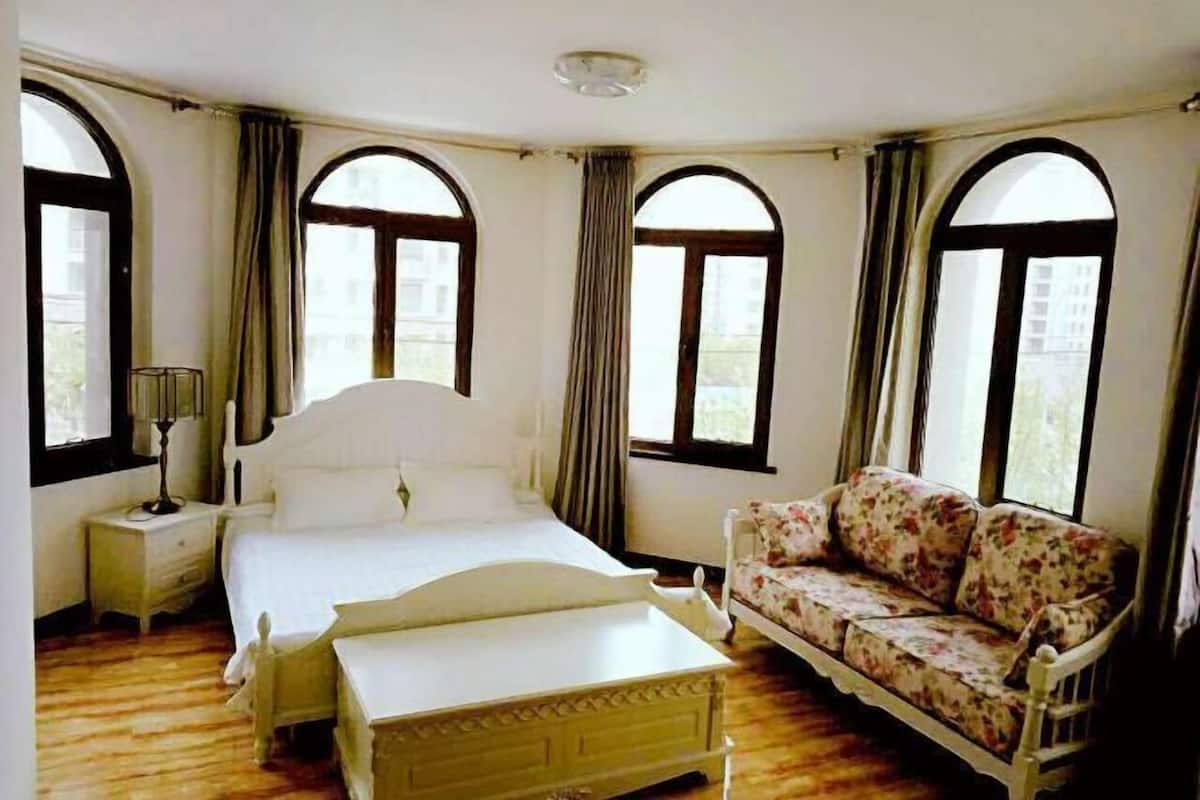 Un dormitorio con cama, mesita de noche, sofá y amplias ventanas de arco.