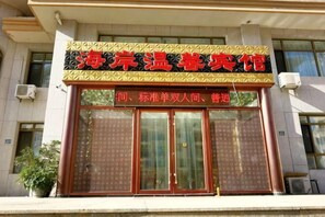 Un edificio con un letrero grande en caracteres chinos, una entrada por puerta de cristal y una planta en maceta a la izquierda.