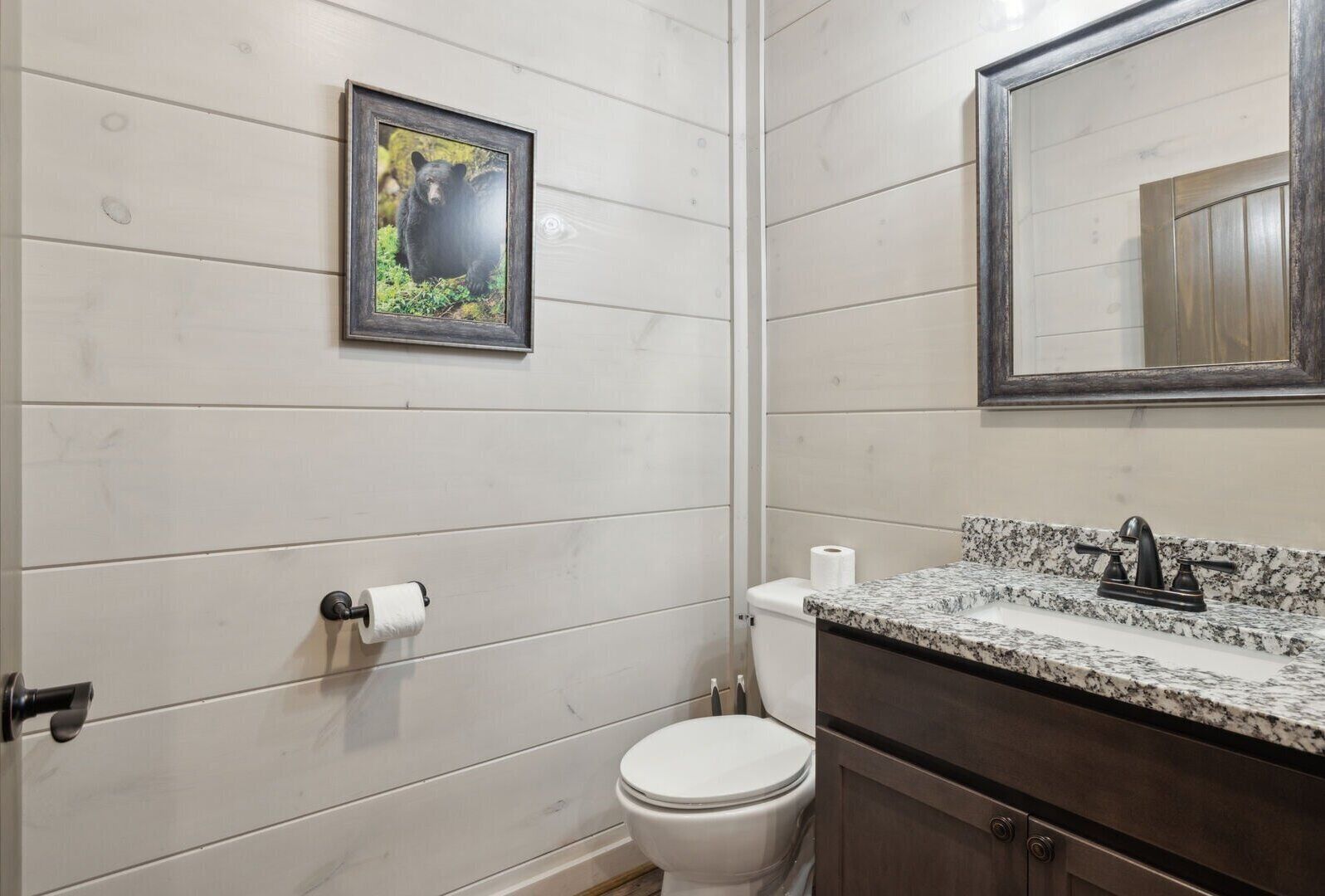 Casa de banho com sanita branca, quadro com urso, bancada de mármore e espelho.