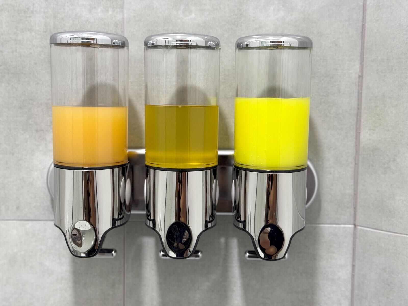 Three stainless steel dispensers with transparent containers filled with different colored liquids.