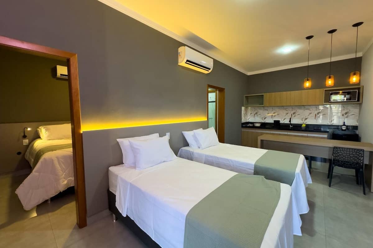 Quarto de hotel com duas camas, uma cozinha compacta e um banheiro.