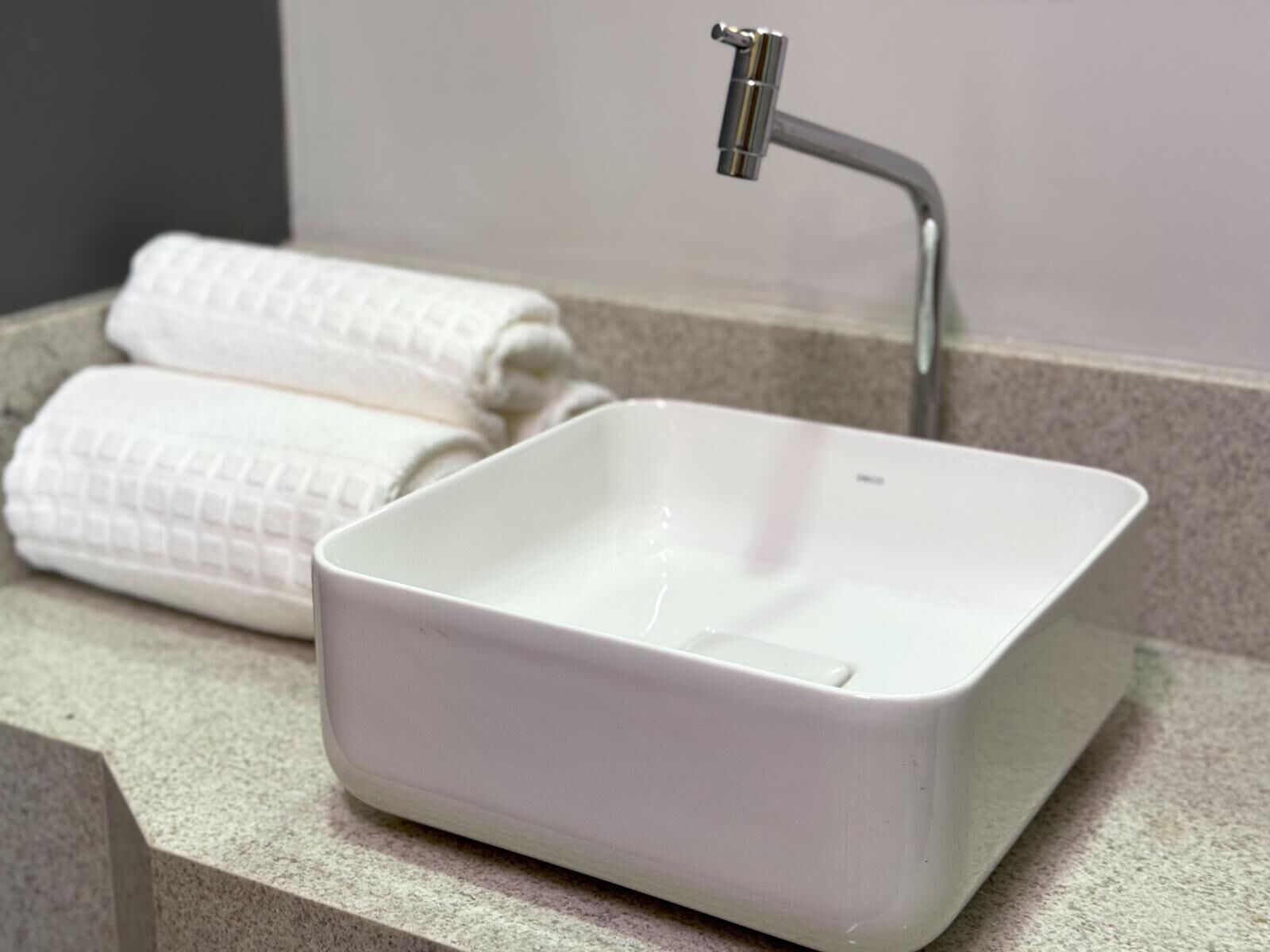 A bathroom with a white rectangular sink, a modern faucet, and two rolled towels on the counter.