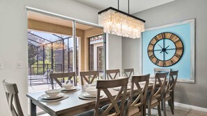 A dining area with a large table set for six, surrounded by wooden chairs with cushioned seats. A large wall clock is mounted on the wall above the table. - 4x TV Wall, Pool Table, EV Charger, Waterpark, 15 Mins to Disney: Grand Getaway (Davenport)