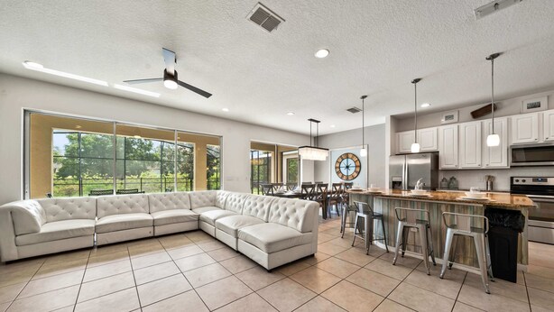 A modern kitchen with a large island, bar stools, and a dining area with a round table. - 4x TV Wall, Pool Table, EV Charger, Waterpark, 15 Mins to Disney: Grand Getaway (Davenport)