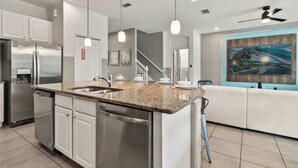 A modern kitchen with a granite countertop, stainless steel appliances, and pendant lighting. - 4x TV Wall, Pool Table, EV Charger, Waterpark, 15 Mins to Disney: Grand Getaway (Davenport)