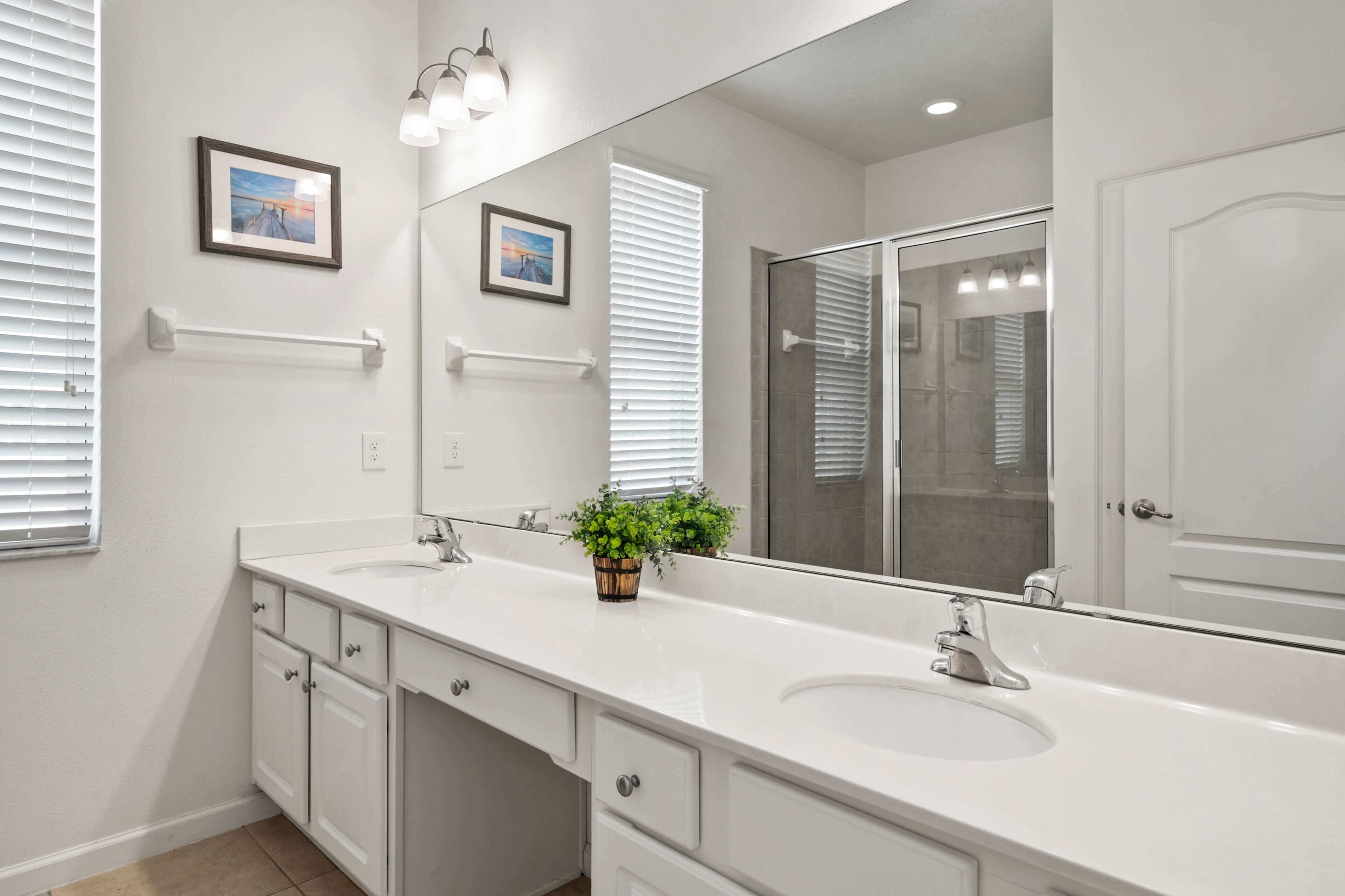 A modern bathroom with two sinks, a large mirror, and a potted plant.
