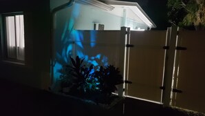 A house with a garage door illuminated by blue light, a window with curtains, and a potted plant in the foreground. -  Streamlined & Chic Getaway Studio in Amazing Sarasota (Sarasota)