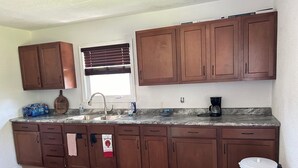 A kitchen with wooden cabinets, a granite countertop, a sink, a coffee maker, and a trash can. - Charming Algoma retreat - 10 min. Walk to the Beach (Algoma)