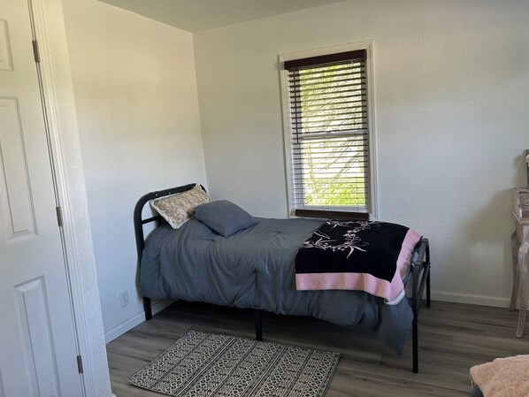 A bedroom with a bed, a window with blinds, a patterned rug, and a wooden dresser.