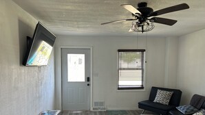 A living room with a ceiling fan, a black leather sofa, a wooden coffee table, and a TV mounted on the wall. - Charming Algoma retreat - 10 min. Walk to the Beach (Algoma)
