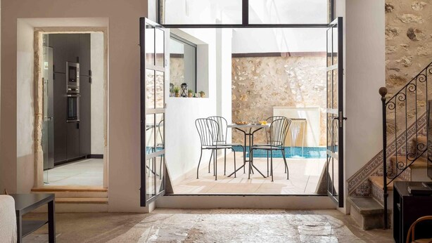 An open doorway leading to a dining area with a pool, stone walls, and a staircase.