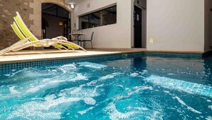 An indoor swimming pool with clear blue water, a lounge area with yellow and green chairs, and a stone wall.